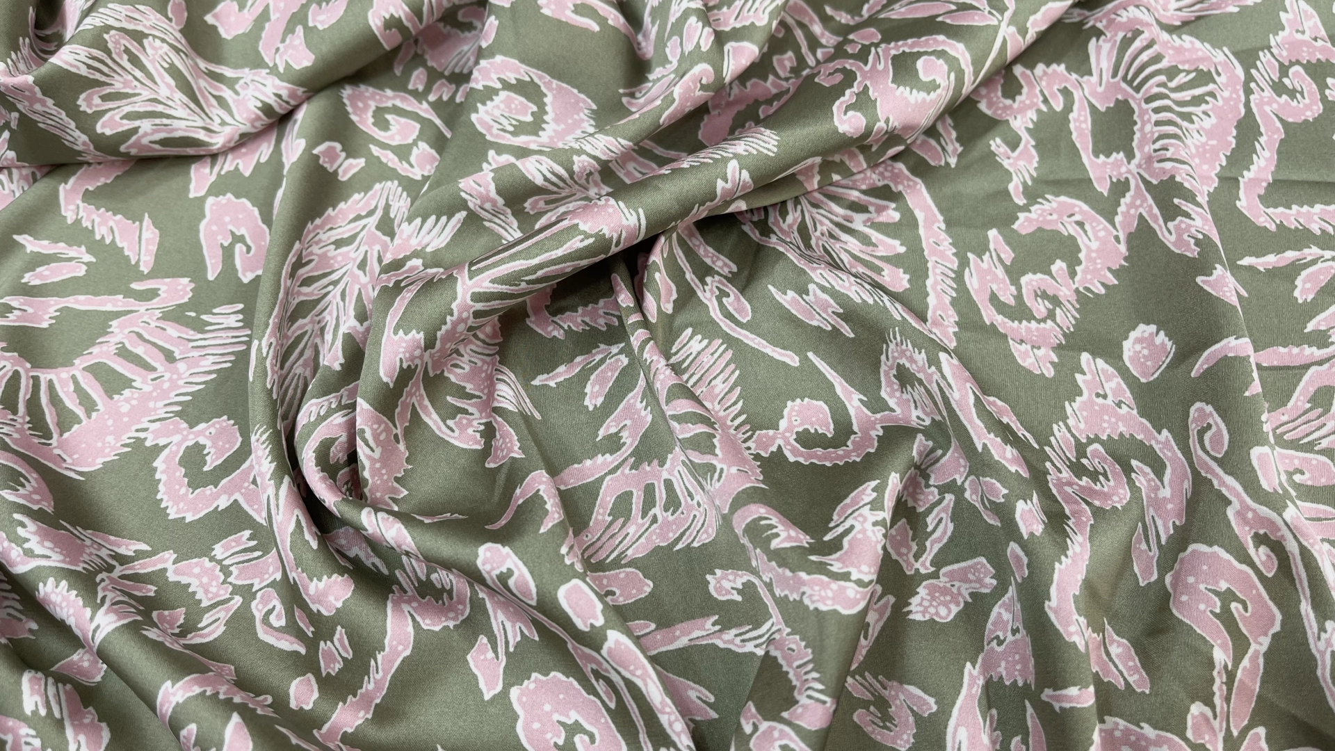 Атлас с торговым названием Армани спокойного оливкового цвета с орнаментом розового цвета. Атлас тактильно очень приятный и мягкий, струящийся с матовым переливом. Идеально подходит для пошива рубашки или платья.