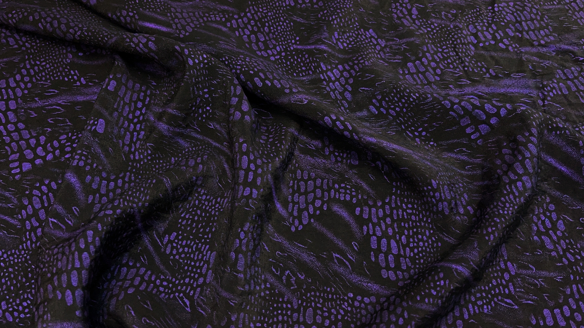 Очень красивая плательная ткань с фиолетовым принтом на черно-графитовом фоне. Фиолетовые фрагмены не сильно яркие, но на контрасте кажутся слегка подсвеченными изнутри. По характеру полотно с формоустойчивым эффектом, но не жесткое. Легкая полупрозрачность на просвет. Самое идеальное применение это рубашка или блузон с пышными фрагментами типа широких пристроенных рукавов.