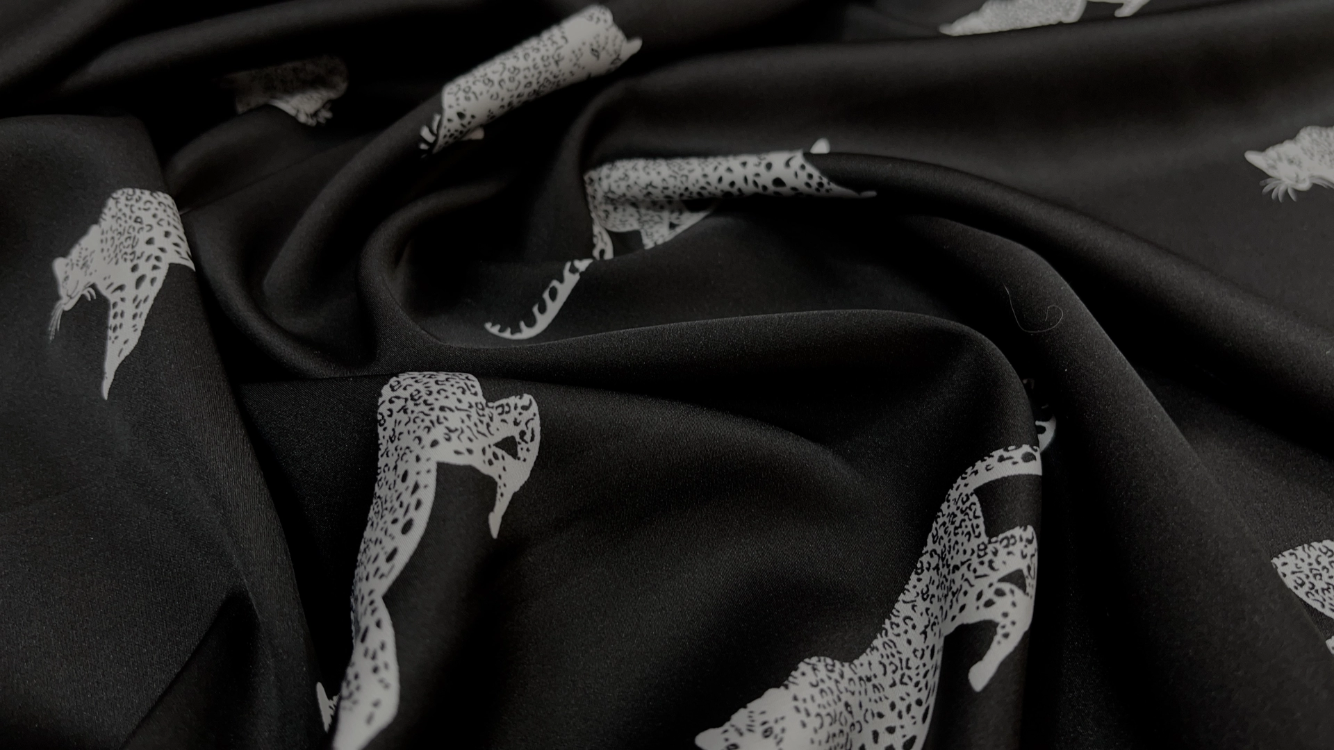Атлас с торговым названием Армани, на черном фоне белые леопарды. Тактильно атлас очень приятный, мягкий и струящийся. Идеален для пошива рубашки или платья.